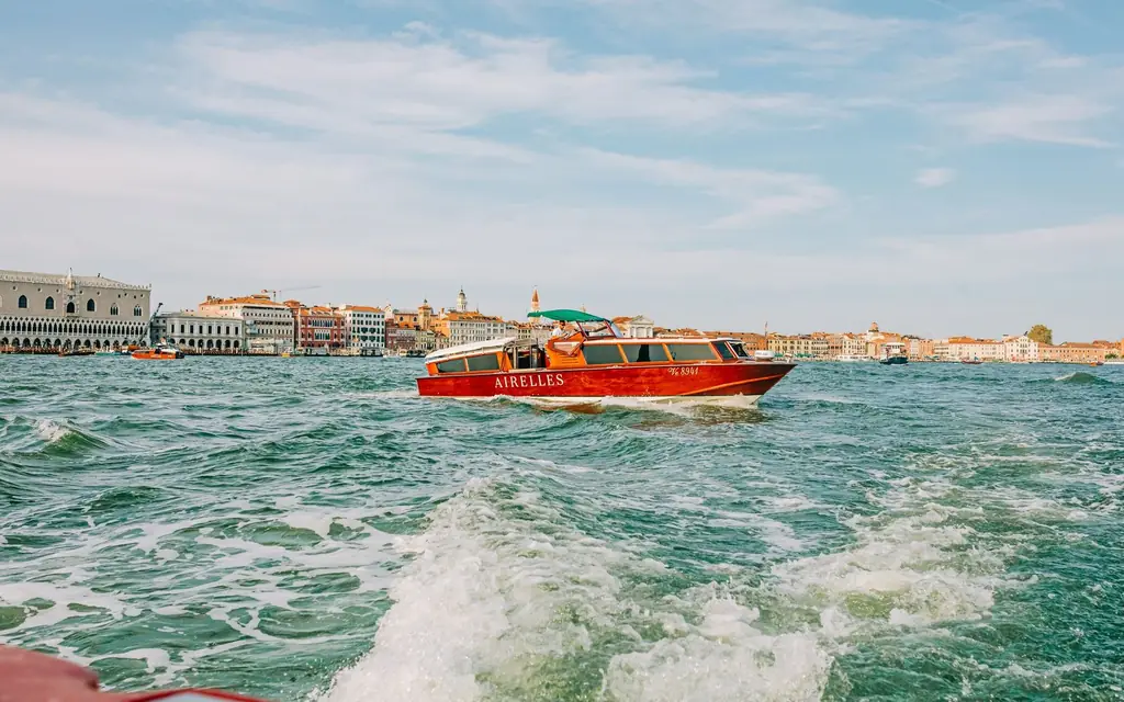 A vibrant red water taxi cruises through the canals of Venice on a sunny day, showcasing the city's iconic architecture.