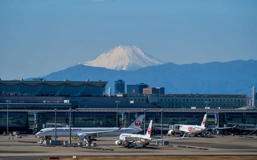 A bustling scene at Haneda Airport with airplanes and Mount Fuji in the background.