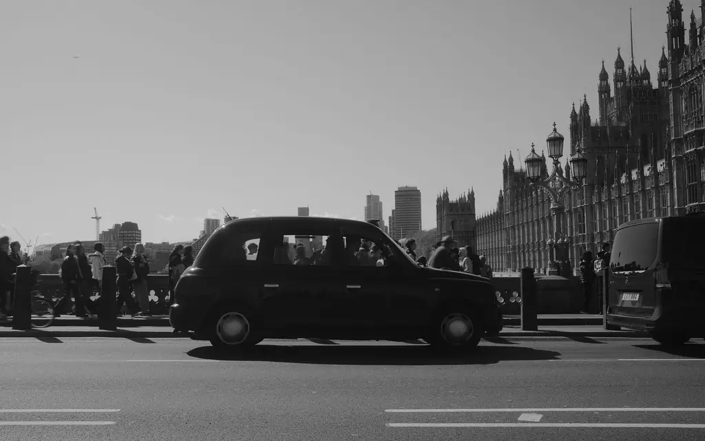 Black cab passing Westminster Bridge with Houses of Parliament, London backdrop.
