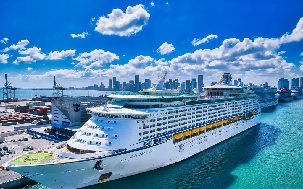 A luxurious cruise ship moored at the bustling Miami port with the city skyline in the background.