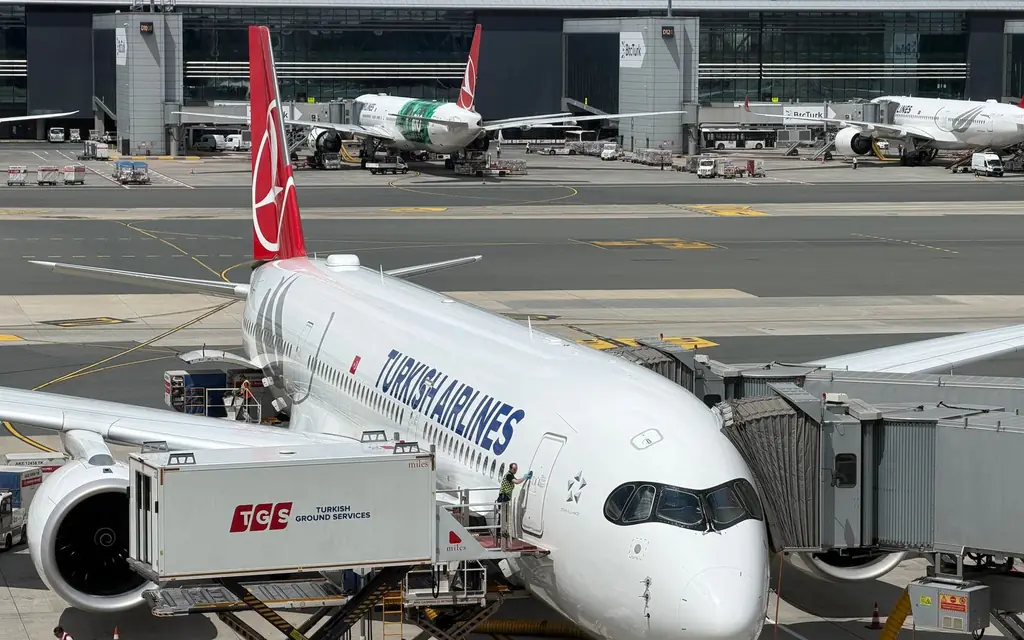 A Turkish Airlines plane docked at Istanbul Airport with various airport services in action.