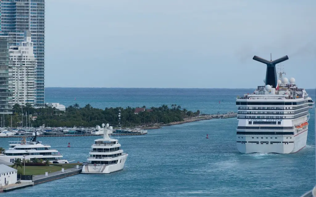 Cruise ship sailing through an urban harbor with city skyline and yachts visible.