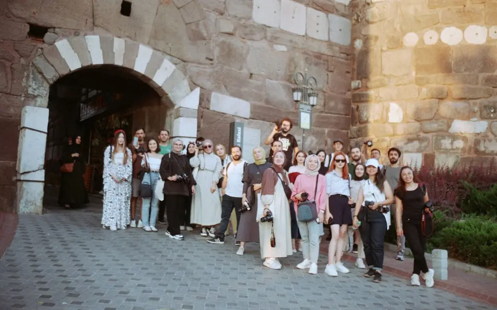 A group of tourists pose at a historic stone city gate, capturing a memorable travel moment.