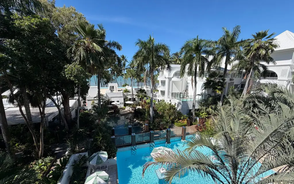 Aerial view of a tropical resort pool area with palm trees and ocean view.